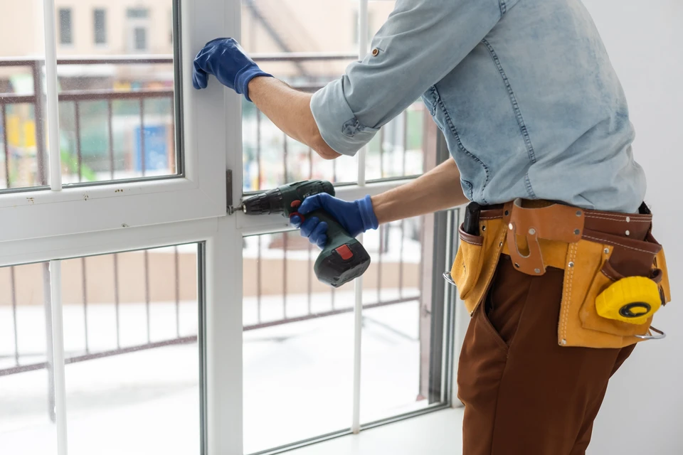 Scène extérieure sous ciel bleu : ouvrier en vêtements de travail et gants noirs installe une verrière sur structure métallique