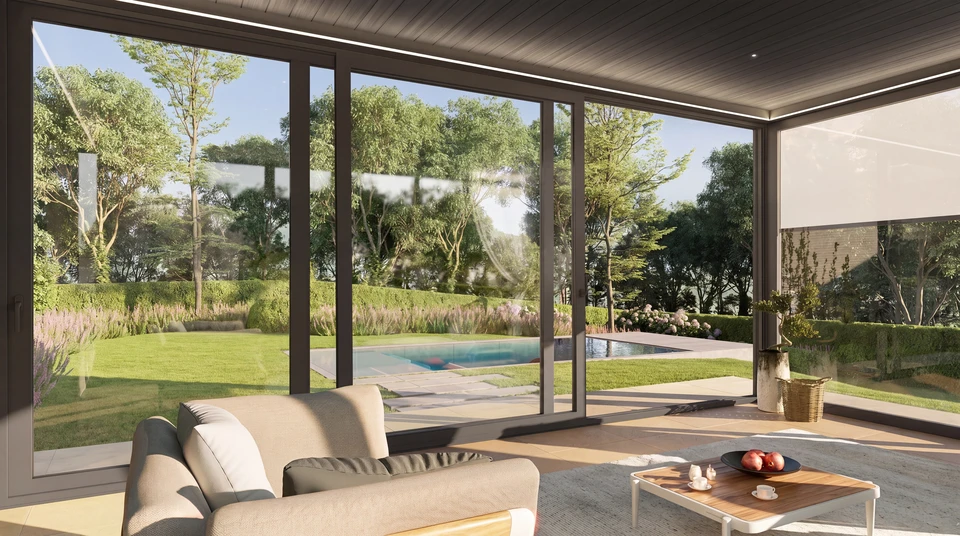 Extension vitrée moderne accolée à une maison ancienne en pierre, pergola bioclimatique à toiture plate anthracite avec lames orientables, structure aluminium thermolaqué, vitrage coulissant grande hauteur, terrasse en dalles grès cérame, salon de jardin résine tressée, arbre ornemental en fleurs roses