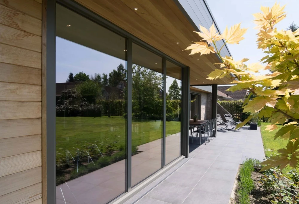 Véranda moderne en aluminium anthracite, structure à toit plat avec couvertine métallique et gouttière intégrée