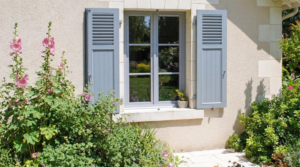 Façade extérieure d'une maison en briques rouges avec trois volets roulants blancs fermés, sous un ciel bleu dégagé