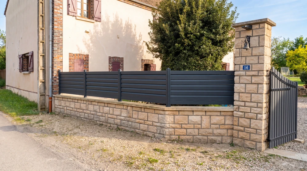 Entrée de propriété résidentielle avec portail coulissant et portillon en aluminium laqué anthracite (RAL 7016), montés sur piliers en pierre de taille apparente
