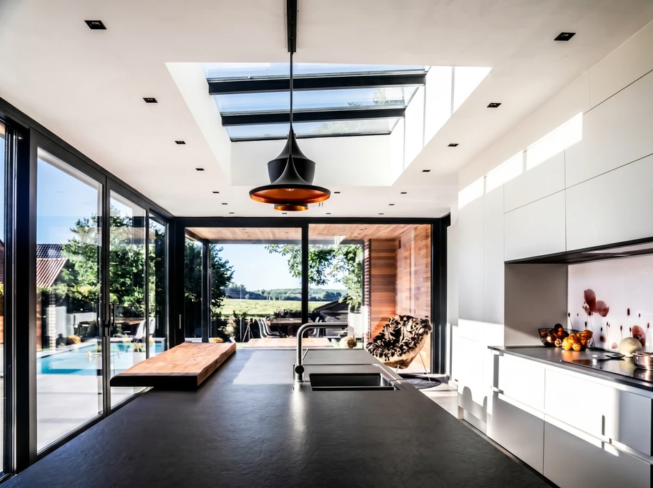 Photographie réaliste d'une cuisine moderne ouverte sur un espace de vie, avec une porte-fenêtre coulissante multi-vantaux en aluminium offrant une vue panoramique sur une terrasse et le jardin. La porte doit être grande ouverte, révélant la continuité sérénité entre l'intérieur et l'extérieur, avec un design contemporain épuré et un excellent rendu des menuiseries. L'éclairage naturel doit mettre en évidence la qualité et la transparence des vitres.